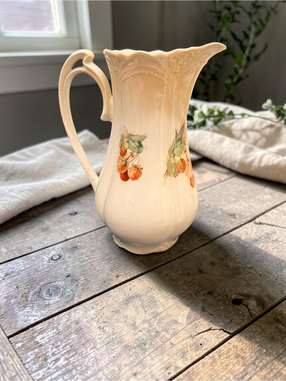 A vintage porcelain pitcher with hand-painted strawberries and a scalloped rim.